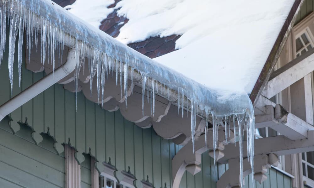 Icicles forming along a snow-covered roof edge due to ice dam buildup on a residential home