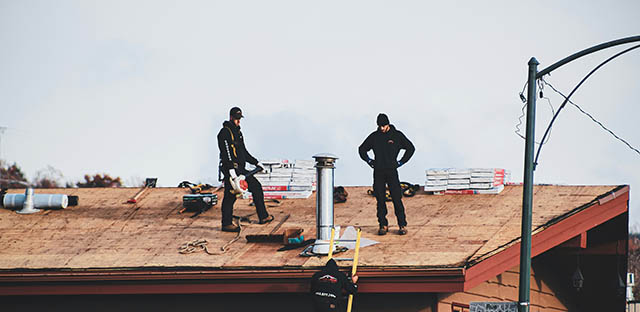 Two construction workers stand on a wooden rooftop