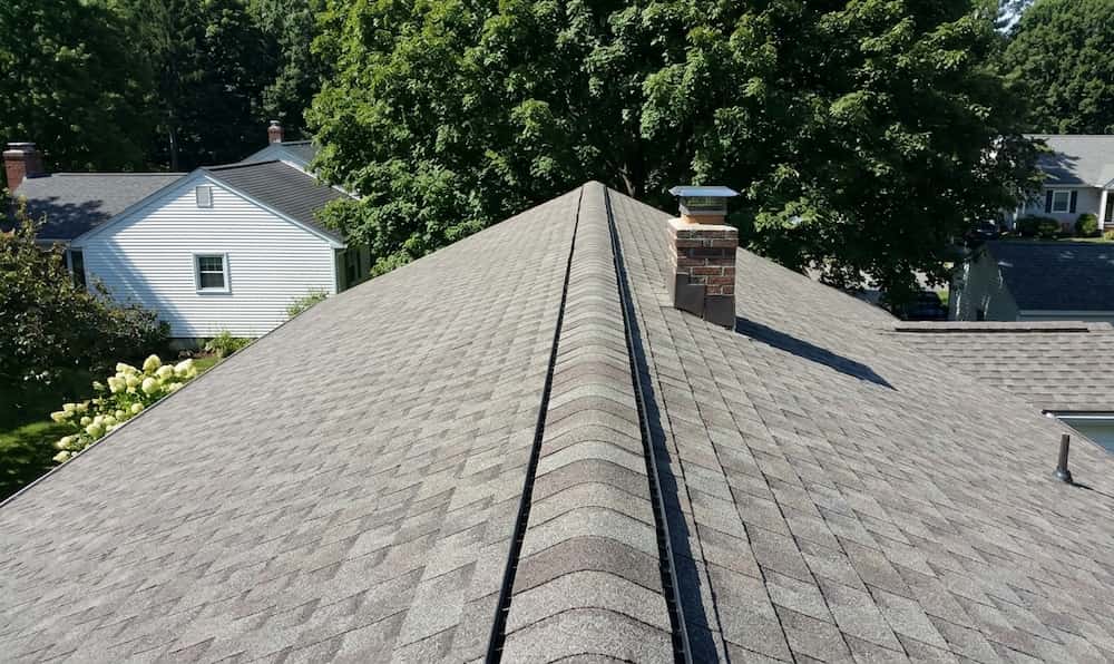 High-angle view of a grey shingled gabled roof with a brick chimney and ridge vent