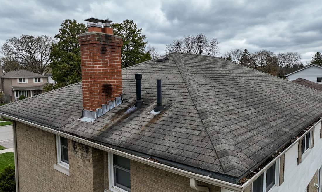 A residential roof with a chimney and vent pipes