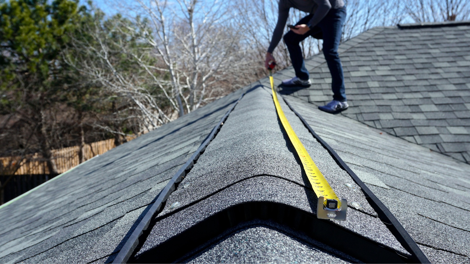 A worker measuring a shingled roof ridge