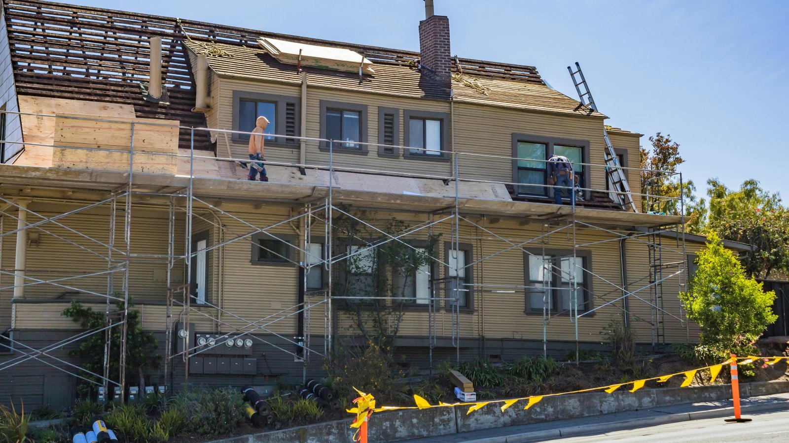 House under renovation with scaffolding and workers fixing the roof on a sunny day