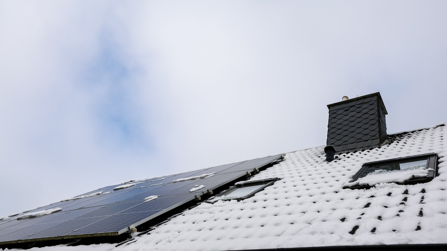 snow-covered shingle roof with a dark slate chimney