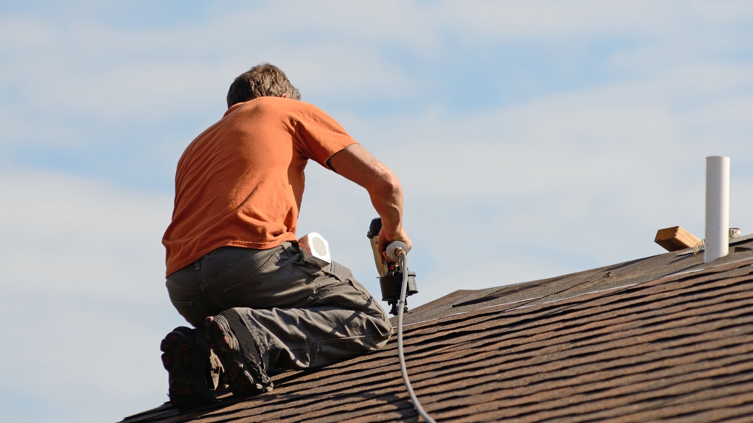 A roofer uses a nail gun on a shingle roof