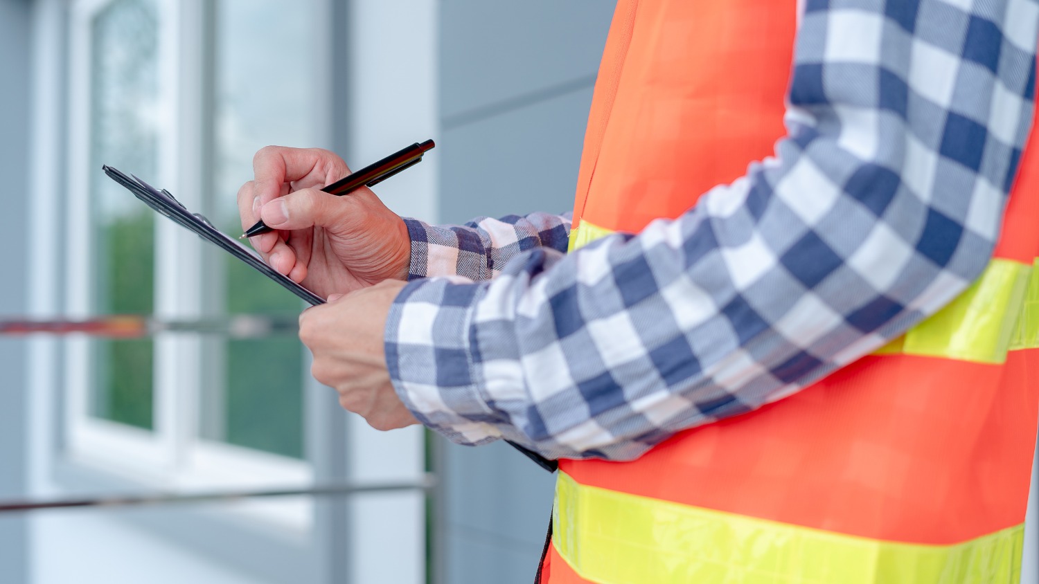 Worker in a safety vest writing on a clipboard