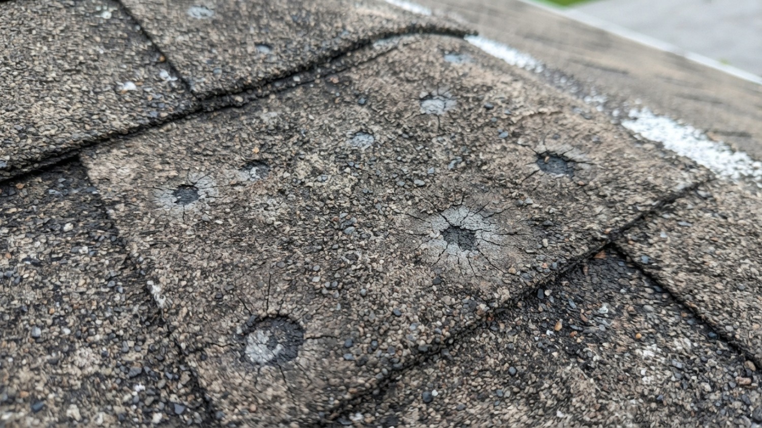 circular hail impact damage on weathered asphalt roof shingles