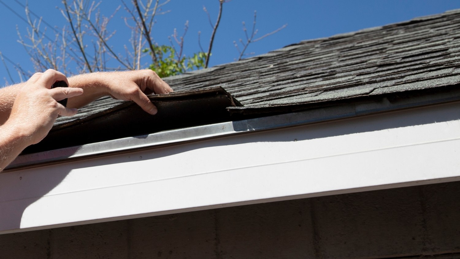 lifting up a damaged section of dark roof shingles