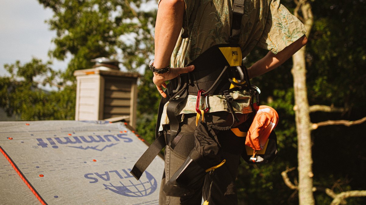 Construction worker wearing safety harness on a rooftop with professional safety gear.