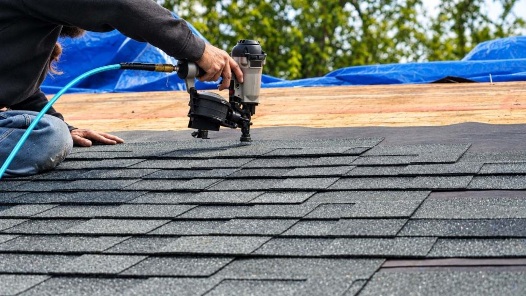 roofer uses a pneumatic coil nailer to install grey architectural shingles