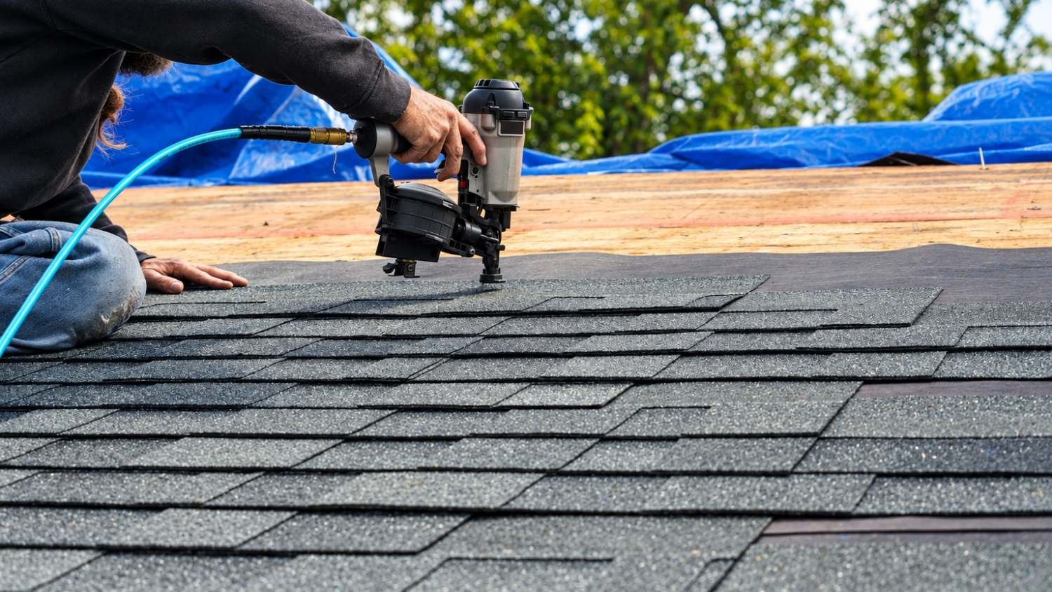 roofer uses a pneumatic coil nailer to install grey architectural shingles