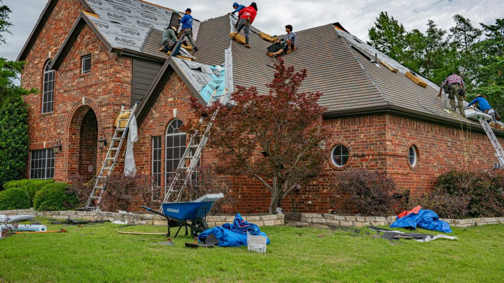 Roofers working on a brick home installing shingles and roofing materials