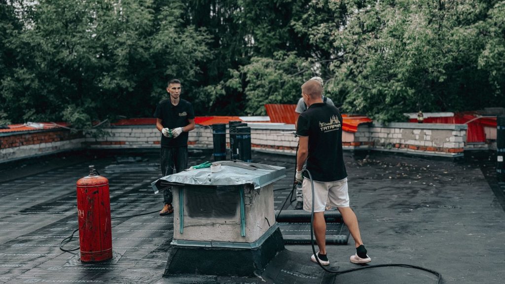 Two commercial roofing contractors performing maintenance on a flat roof with equipment and tools