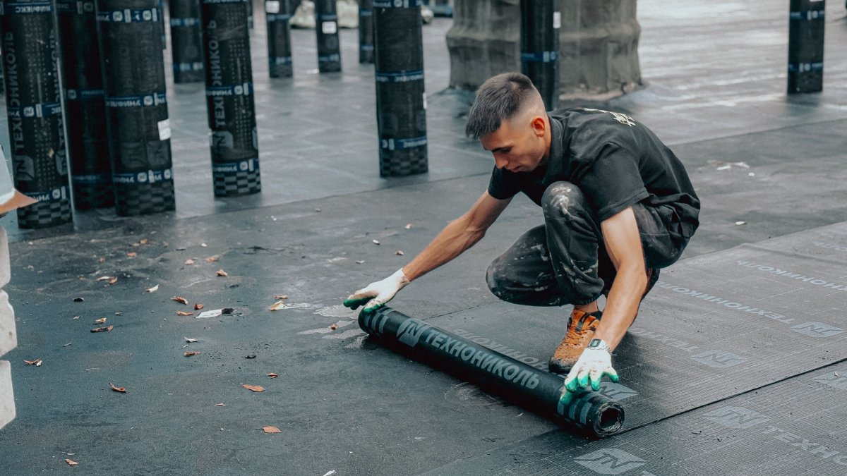 Construction worker applying waterproof membrane on flat commercial rooftop to protect against weather