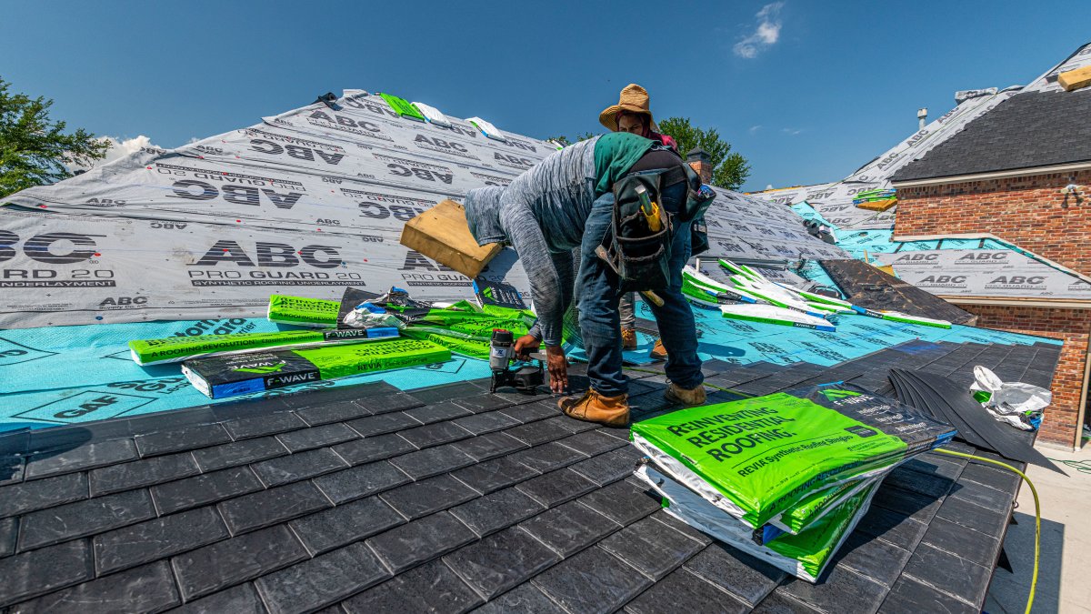 Workers installing a synthetic slate roof on a brick house, focusing on roof-to-wall intersections.